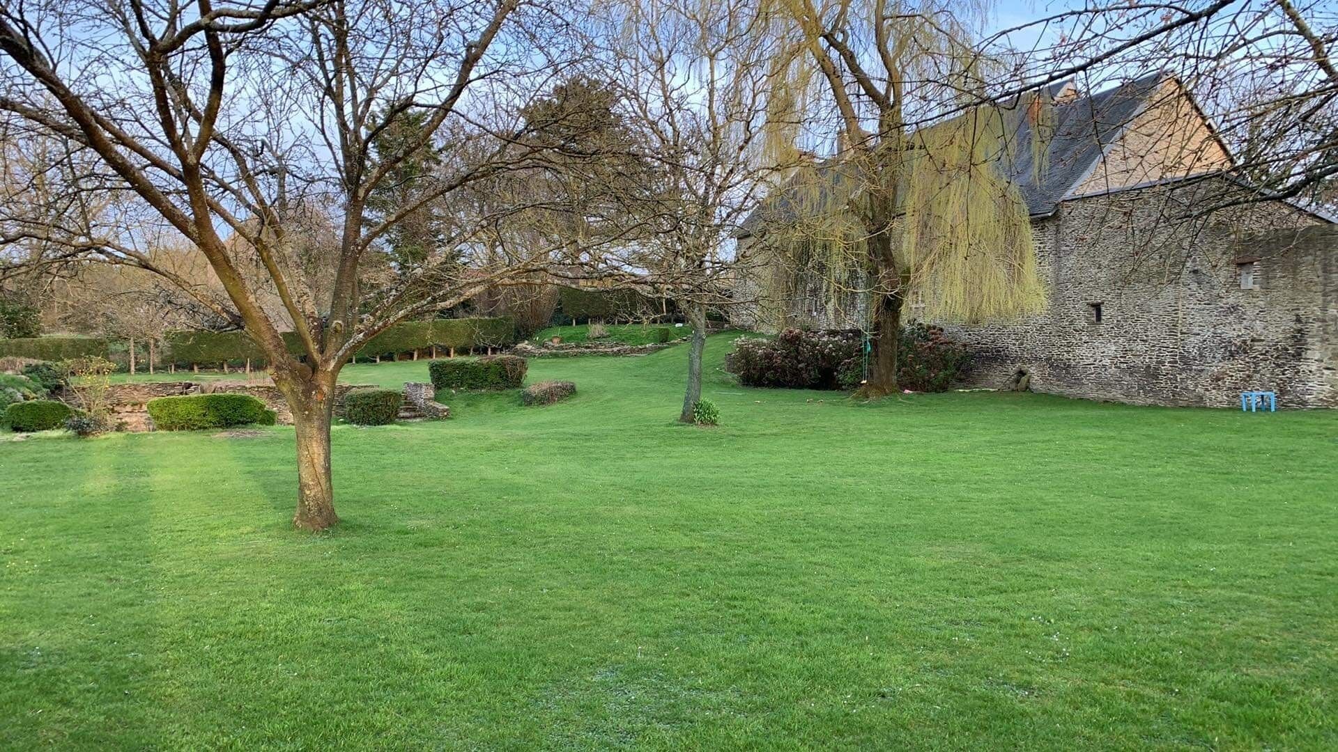 Un bâtiment en pierre avec une cour verdoyante et des arbres.