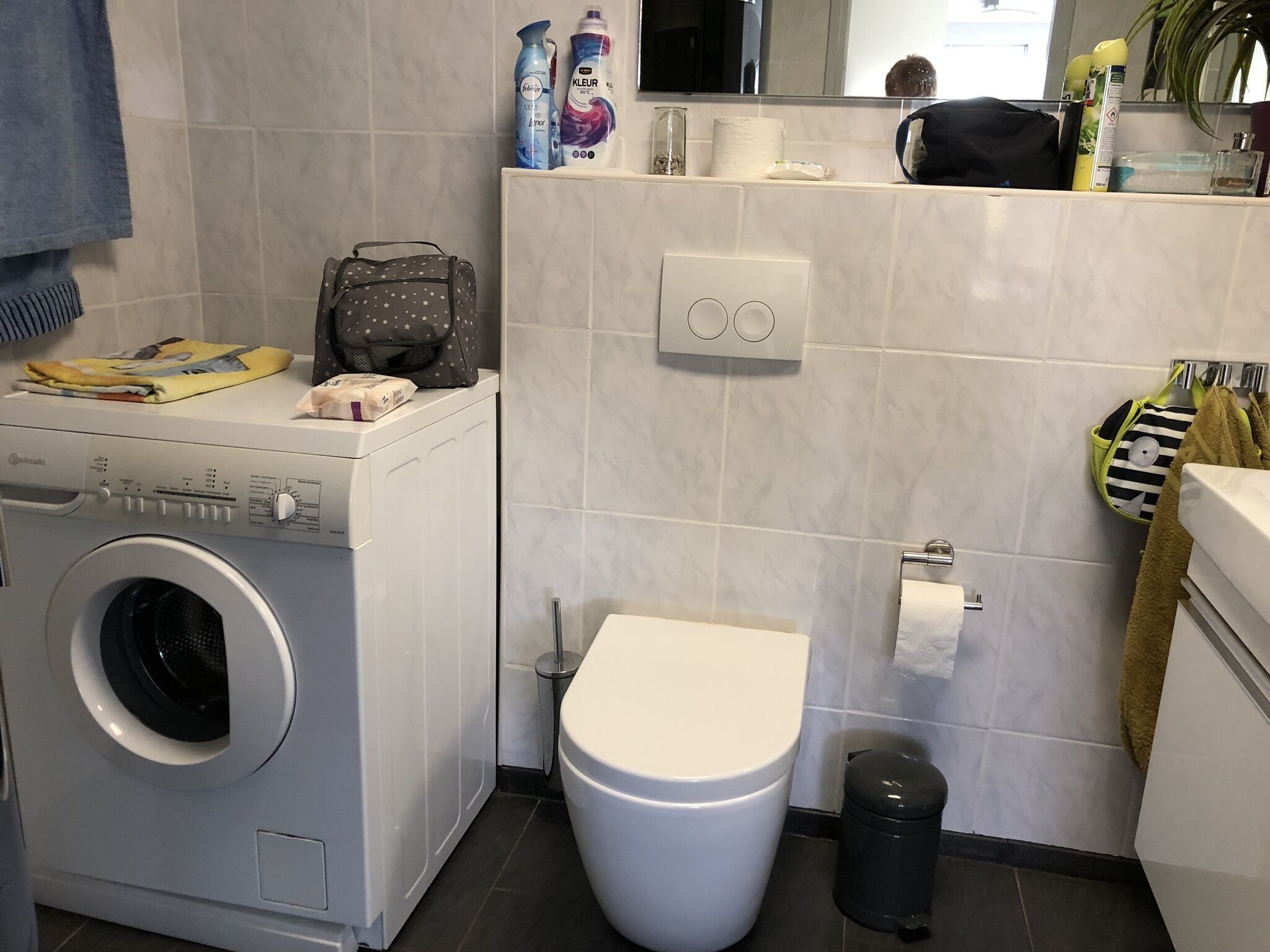 Une petite salle de bain équipée d’un lave-linge, de toilettes et d’une petite poubelle.