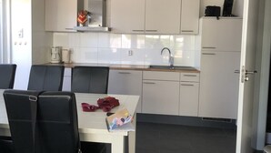 Une cuisine moderne avec des meubles blancs, une hotte en acier inoxydable, un évier et un coin repas comprenant une table et des chaises.