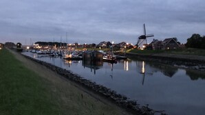 Un canal avec des bateaux, un moulin à vent et des maisons en arrière-plan.