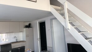 Une cuisine moderne avec des meubles blancs, un four encastré et un évier. Un escalier mène à une pièce sombre.
