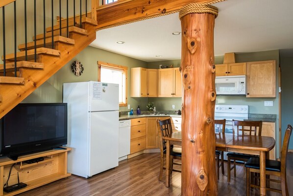 Una cocina con armarios de madera, un refrigerador, un microondas, una mesa de comedor con sillas y una escalera de madera.