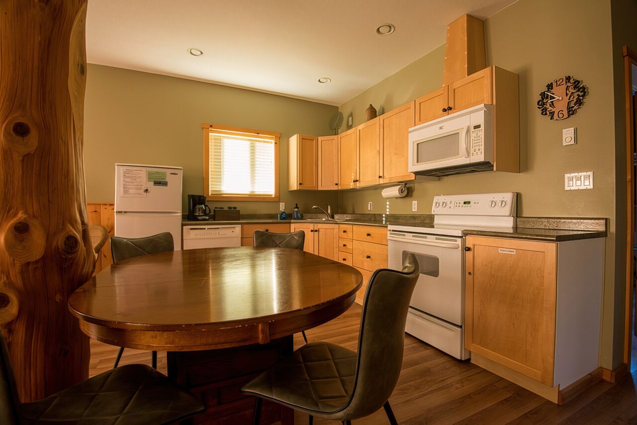 Una cocina compacta con armarios de madera, microondas, horno y un comedor con mesa redonda y sillas.