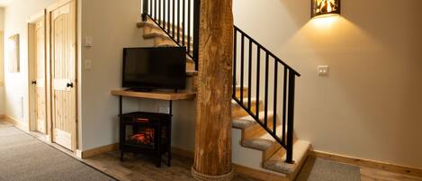 Una escalera con un pilar de madera, un televisor sobre un soporte y una lámpara fijada a la pared.
