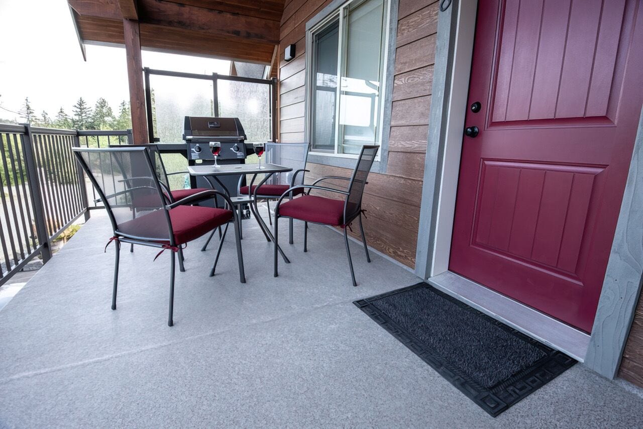 Un patio al aire libre con una parrilla, cuatro sillas y una puerta roja.