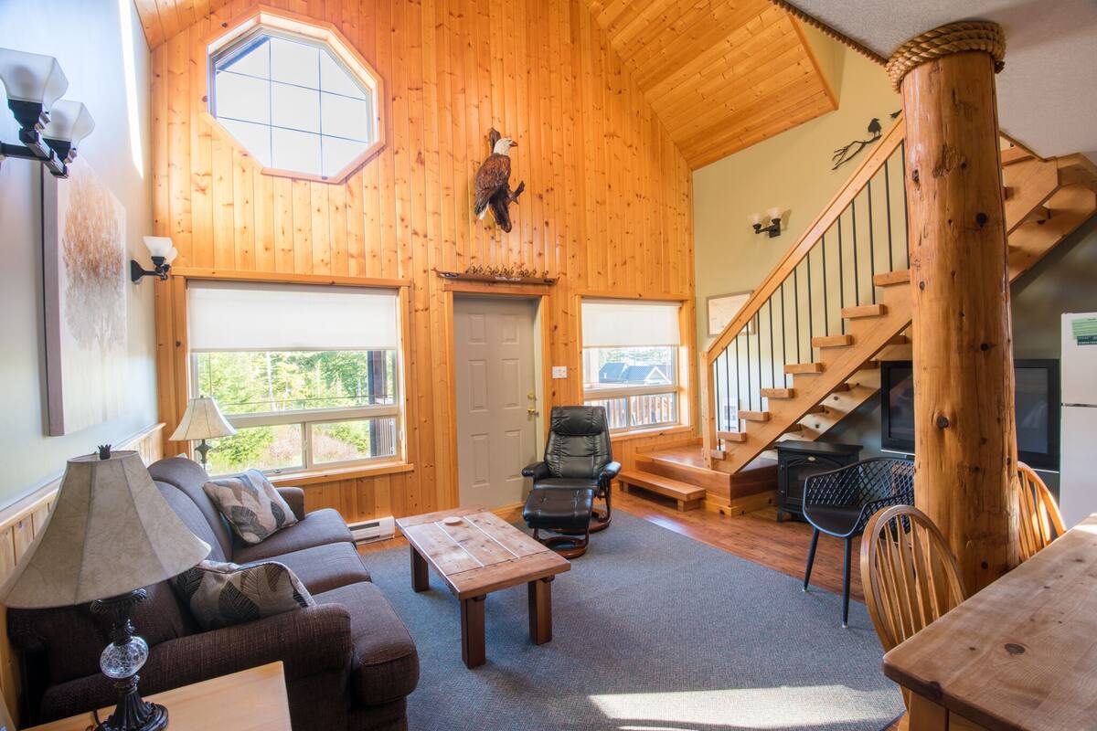A wooden interior with a sofa, a table, a chair, a staircase, and a mounted bird.