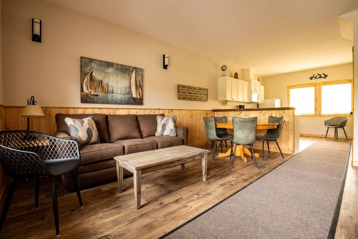 A cozy living room with a wooden floor, a brown sofa, a coffee table, and a dining area with chairs and a table.