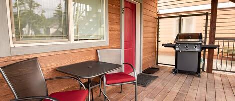 An outdoor patio with a grill, a table, and two chairs.