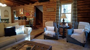 Un interior de cabaña acogedor con sofá, sillones, una mesa de centro y un comedor.