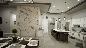 Eine moderne Küche mit weißen Schränken, einer Marmor-Spritzschutzwand und einer Kochinsel mit Barhocker.