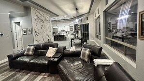 Ein modernes Wohnzimmer mit einer Eckcouch, einer Wandverkleidung aus Marmor und Blick in die Küche.