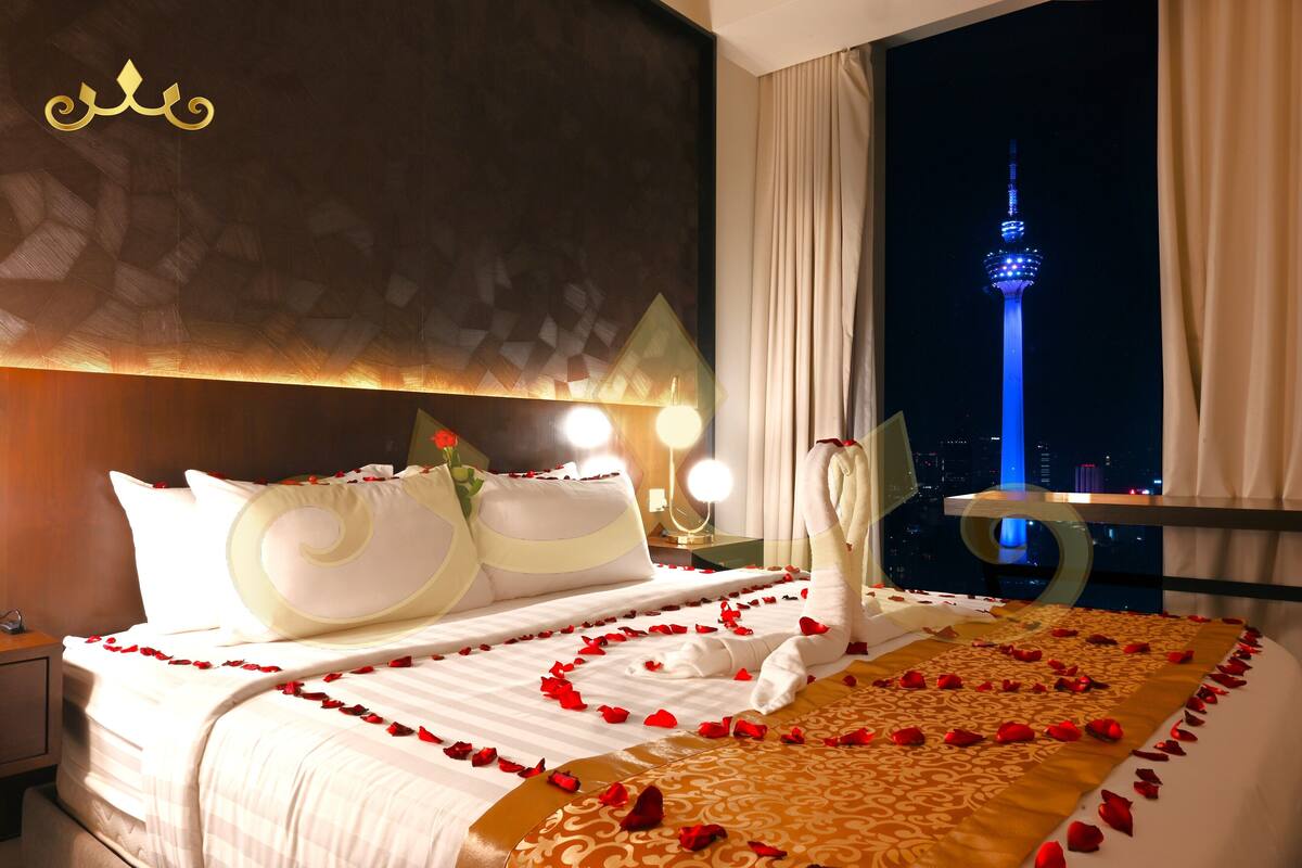 A hotel room with a bed adorned with rose petals, a view of the CN Tower, and a night sky.