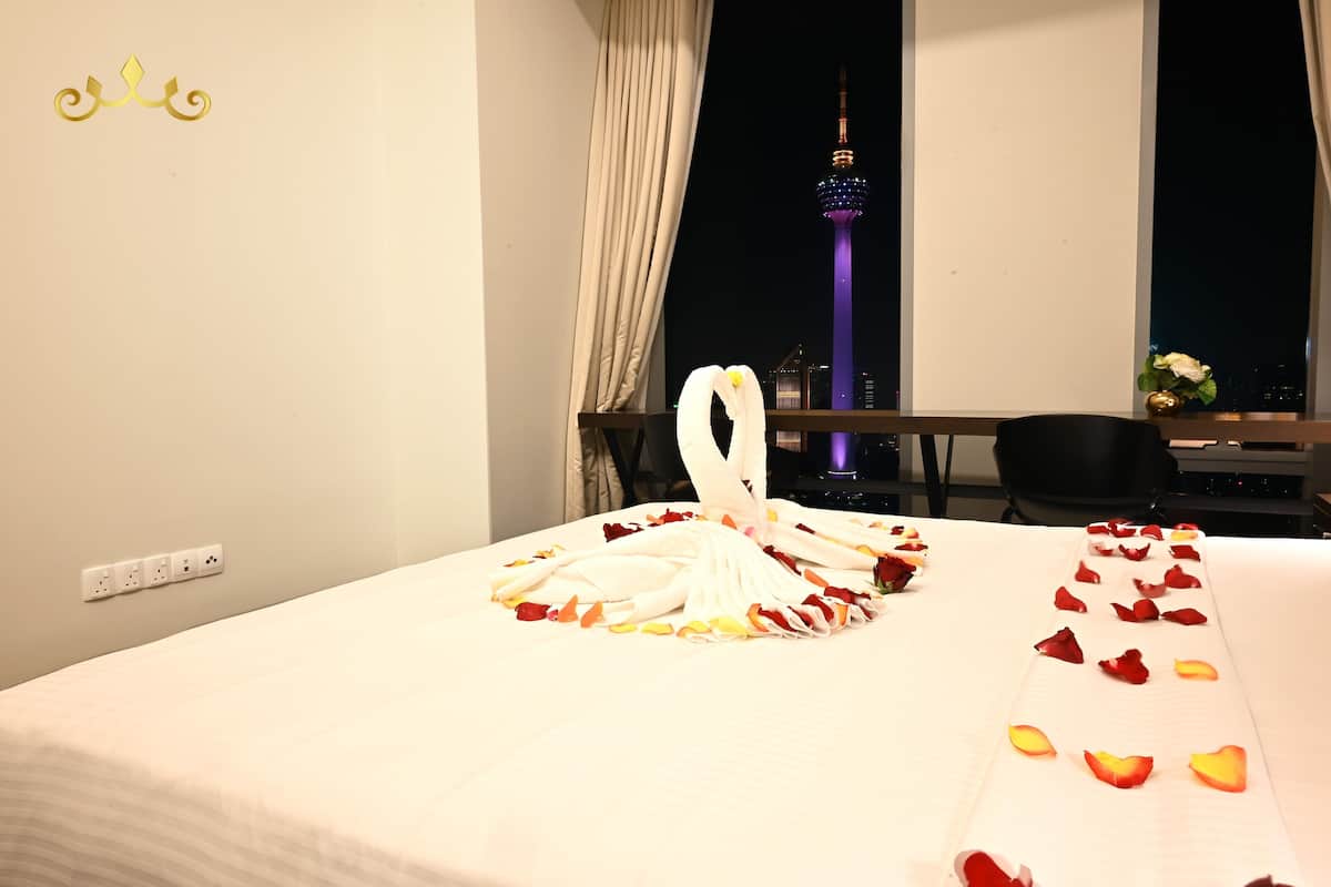 A hotel room with a bed, a desk, and a view of a tower at night.