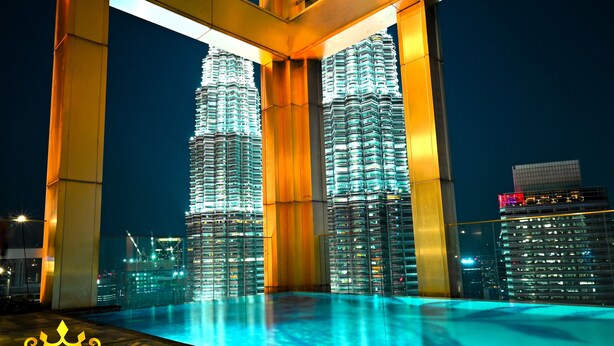A nighttime view of two illuminated skyscrapers with a pool in the foreground. - Tropicana The Residence KLCC Golden Crown (Kuala Lumpur)