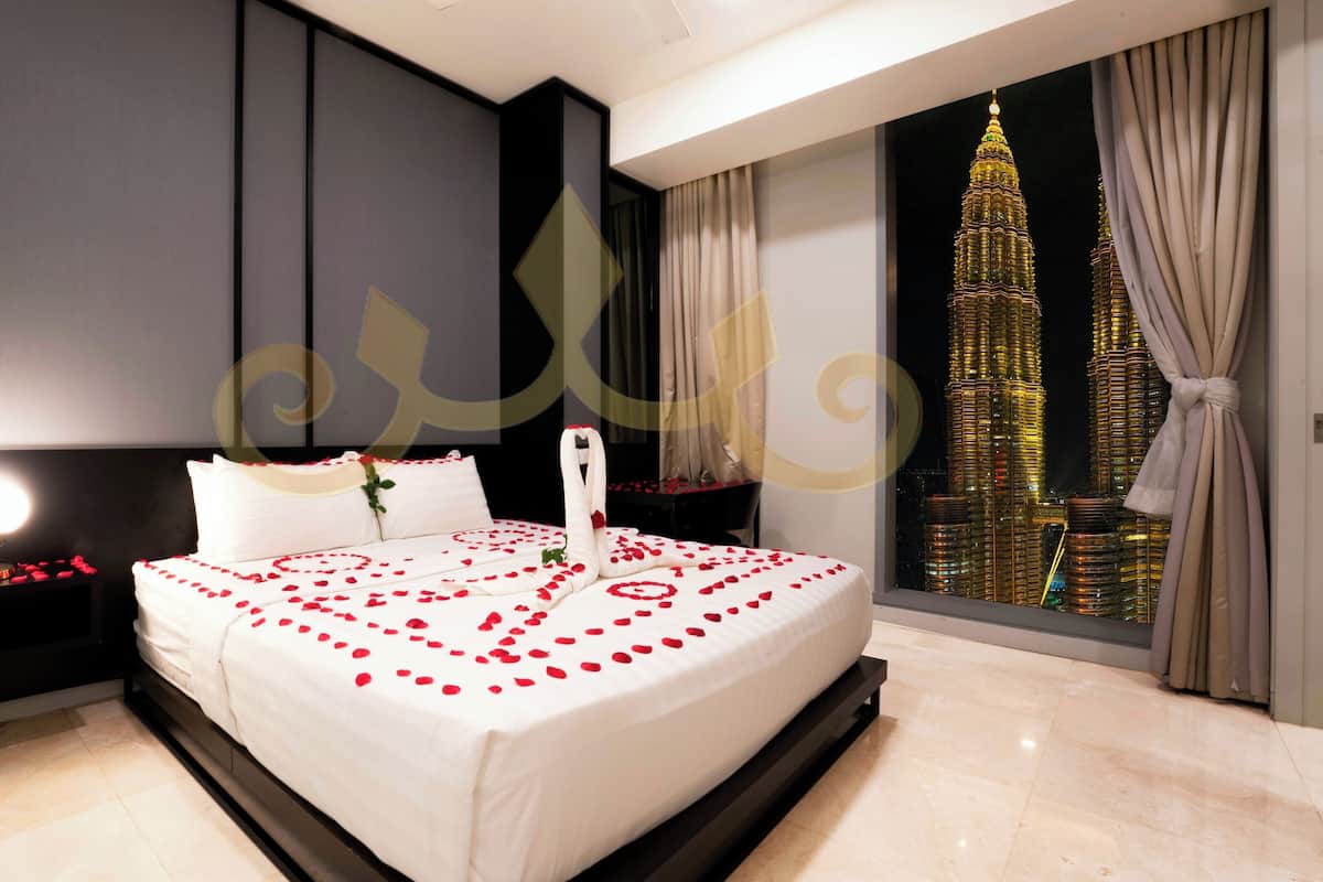 A modern hotel room with a large bed, a nightstand with a lamp, and a view of a tall building.