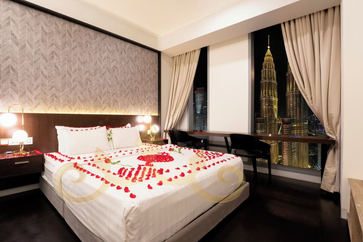 A hotel room with a large bed, bedside lamps, a nightstand, a desk, and a view of a cityscape.