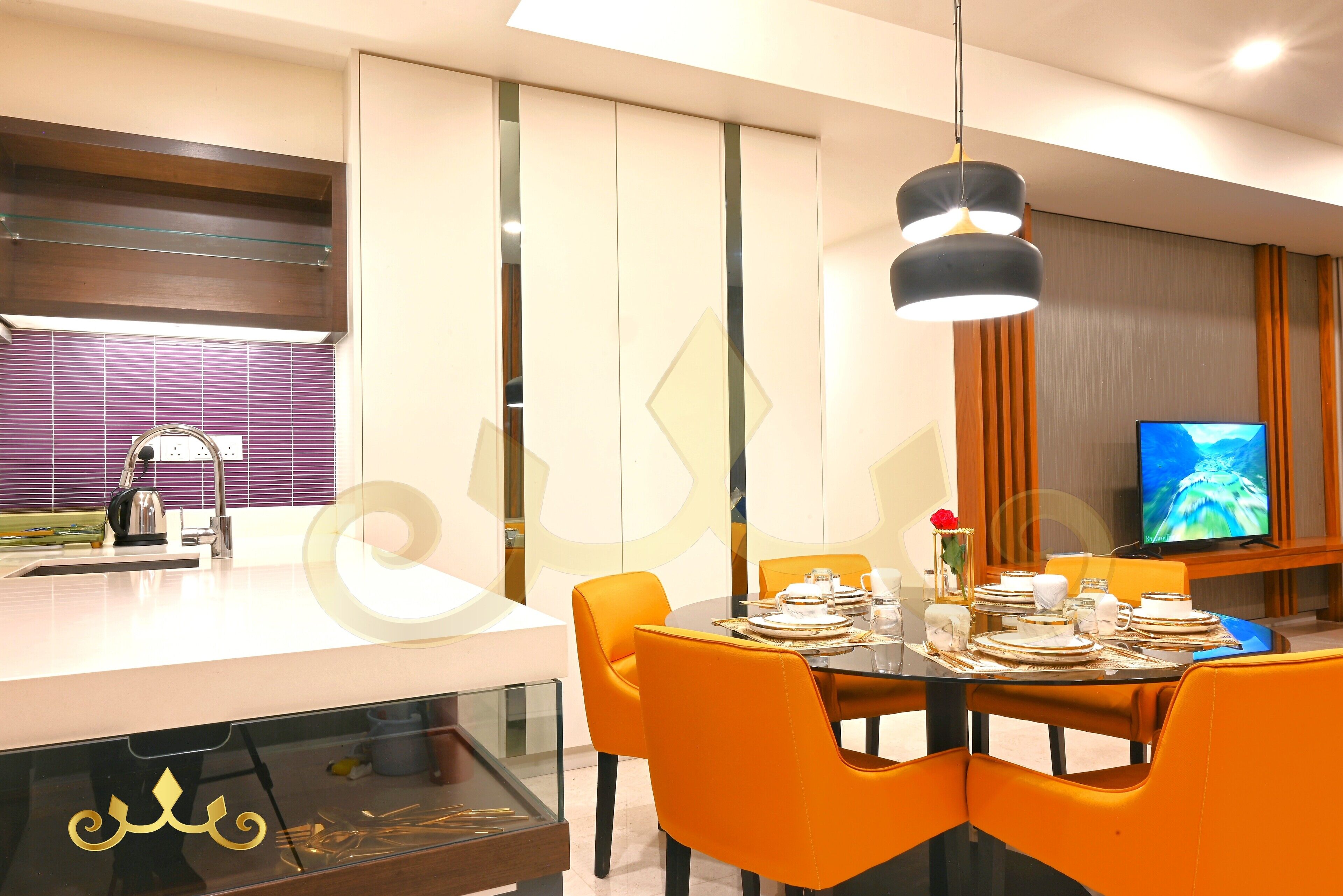 A modern dining area with a glass-top table, orange chairs, and a television in the background.