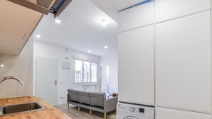 Una cucina compatta con lavatrice integrata, un divano grigio e un piano di lavoro in legno.