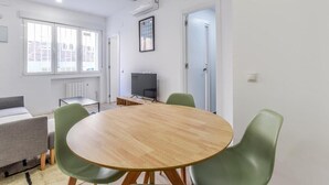 Una stanza moderna con un tavolo rotondo in legno, sedie verdi, un divano grigio, una TV e una finestra con persiane.