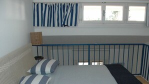A bedroom with a bed, pillows, a window with curtains, and a nightstand.