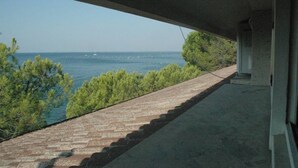 A view from under a building with a paved walkway leading to a body of water, surrounded by greenery.