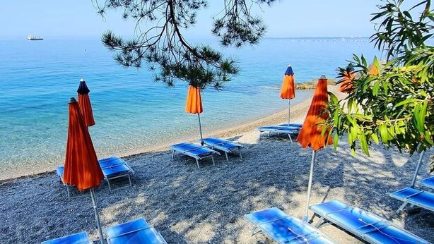 A beachside area with sun loungers and umbrellas, a clear view of the sea, and a ship in the distance.