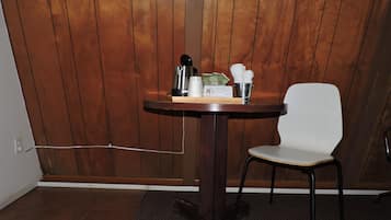 Une petite table avec une chaise, une machine à café, une tasse et un seau rempli de serviettes en papier.