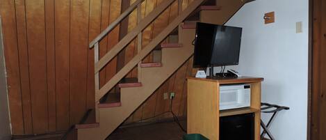 A wooden staircase with a television on a wooden stand and a trash bin.