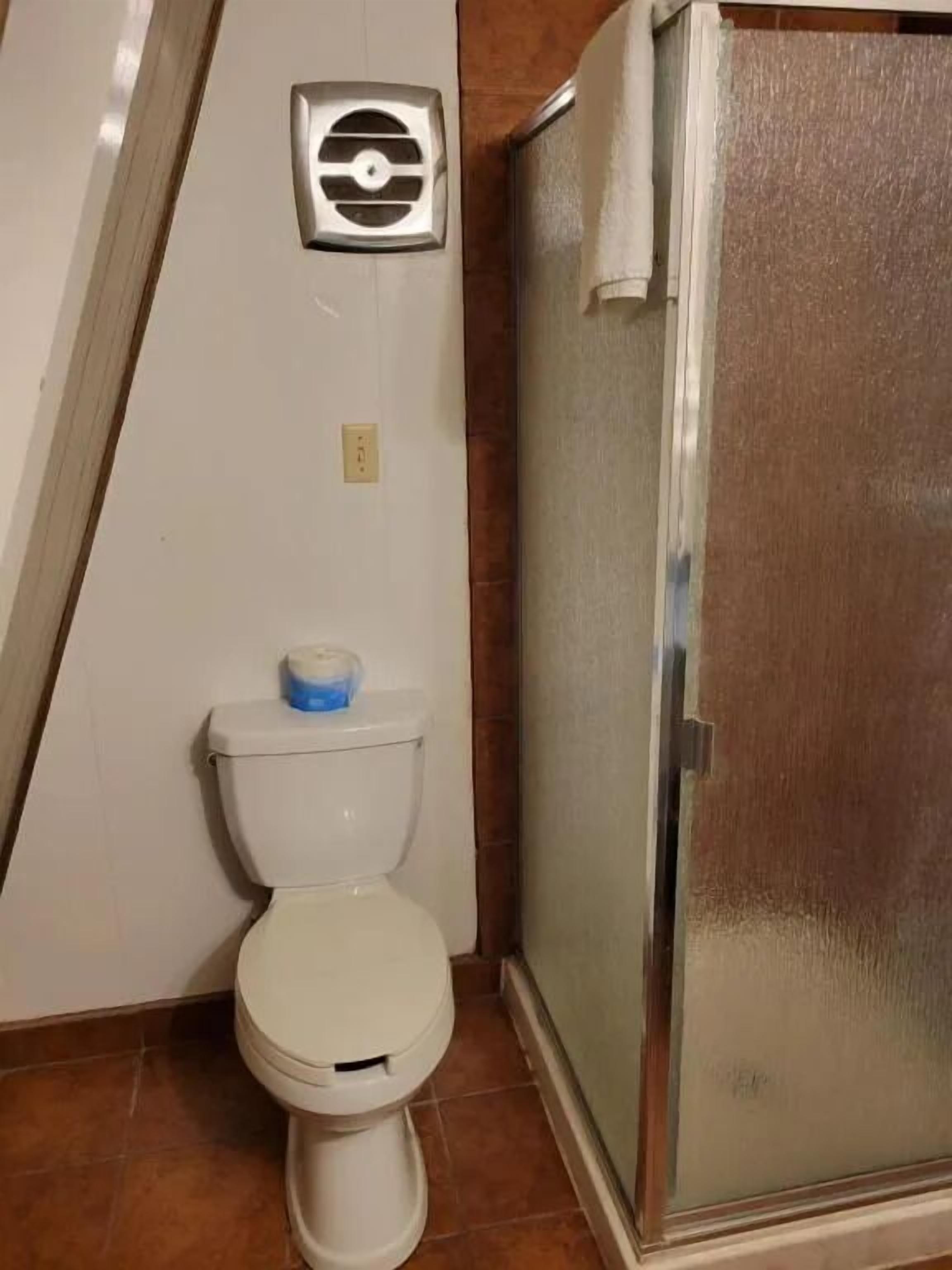 A small bathroom with a toilet, a shower enclosure, and a wall-mounted ventilation unit.