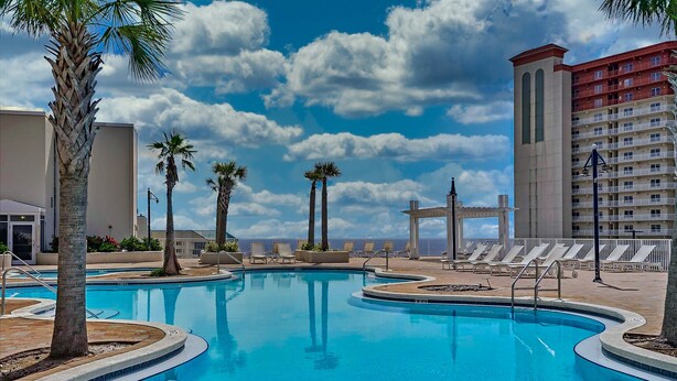 A pool area with lounge chairs and palm trees, surrounded by buildings.