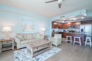 A living room with a sofa, coffee table, and a chair. There is a kitchen area with a refrigerator, microwave, and bar stools. - Excellent Location & Amenities at Laketown Resort - Perfect for Extended Stays.  (Panama City Beach)