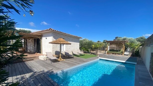 A swimming pool with a wooden deck, a small building with a tiled roof, and outdoor seating. - Charming villa with pool in Bonifacio (Bonifacio)