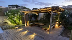 A wooden deck with a pergola and seating area, surrounded by greenery and a view of a house. - Charming villa with pool in Bonifacio (Bonifacio)