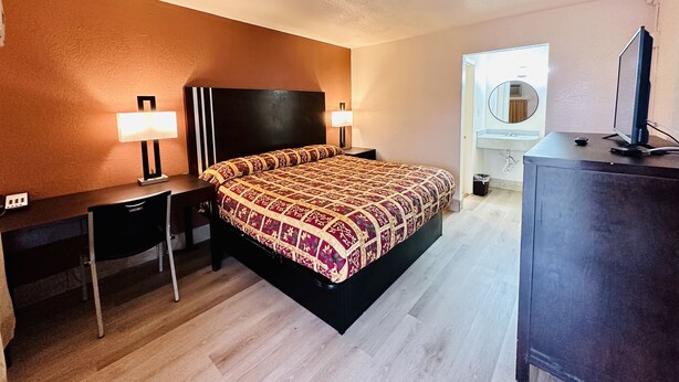 A hotel room with a bed, bedside tables, a desk, a television, and a bathroom with a mirror and sink. - Economy Inn (Houma)