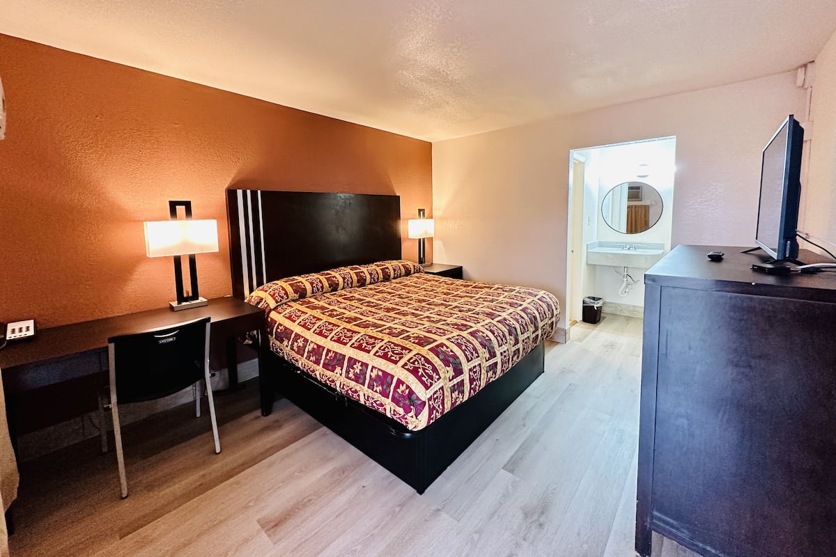 A hotel room with a bed, bedside tables, a desk, a television, and a bathroom with a mirror and sink.