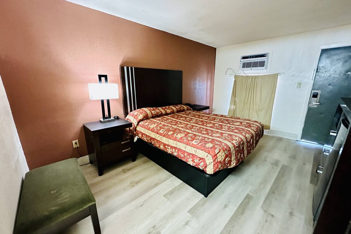 A bedroom with a bed, bedside table, lamp, and a small bench.