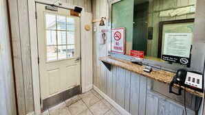 A motel reception area with a wooden interior, a reception desk, a phone, and a window with a view of the outside. - Economy Inn (Houma)