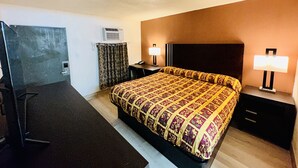 A hotel room with a bed, two bedside tables, a desk, an air conditioning unit, and curtains. - Economy Inn (Houma)
