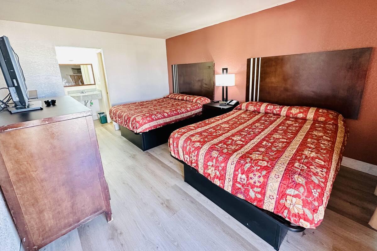 A hotel room with two beds, a desk with a computer, a lamp, and a mirror.