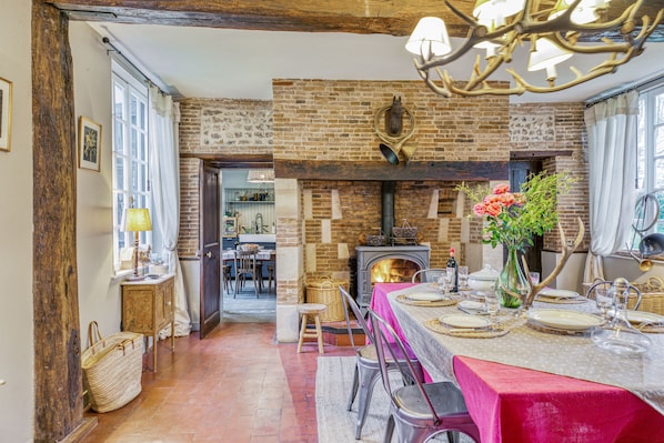A rustic dining area with a brick fireplace, wooden beams, and a chandelier.