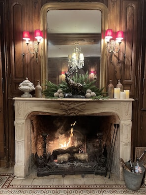 A fireplace with a lit fire, surrounded by decorative items including a deer statue, candles, and a vase.