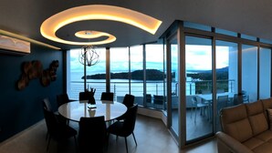 Ein moderner Essbereich mit einem runden Tisch und Stühlen, einer Deckenleuchte und Blick auf ein Gewässer durch große Glasüren.