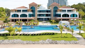 Ein Resort mit mehreren Schwimmbecken, einem Strand und einem großen Hotel im Hintergrund.