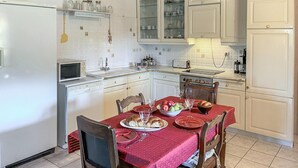 A compact kitchen with white cabinets, a microwave, a sink, and a dining table set with plates, a bowl of fruit, and bread. - 3 bedroom lovely home in Samos (Samos)