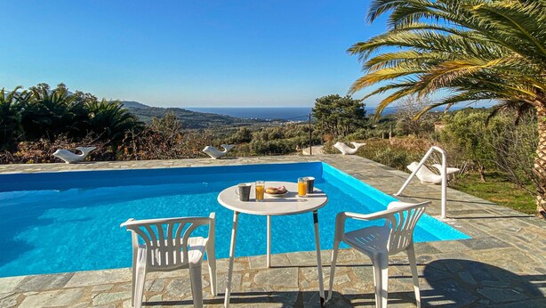 A pool with a clear view of the sea and hills, surrounded by white chairs and a table with drinks. - 3 bedroom lovely home in Samos (Samos)