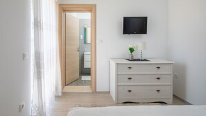 A bedroom with a bed, a dresser with drawers, a television mounted on the wall, and a door leading to a bathroom. - LUXURY APARTMENT 3 BEDROOMS 3 BATHROOMS WITH WHIRLPOOL AND SAUNA (Trogir)