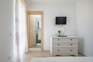 A bedroom with a bed, a dresser with drawers, a television mounted on the wall, and a door leading to a bathroom. - LUXURY APARTMENT 3 BEDROOMS 3 BATHROOMS WITH WHIRLPOOL AND SAUNA (Trogir)