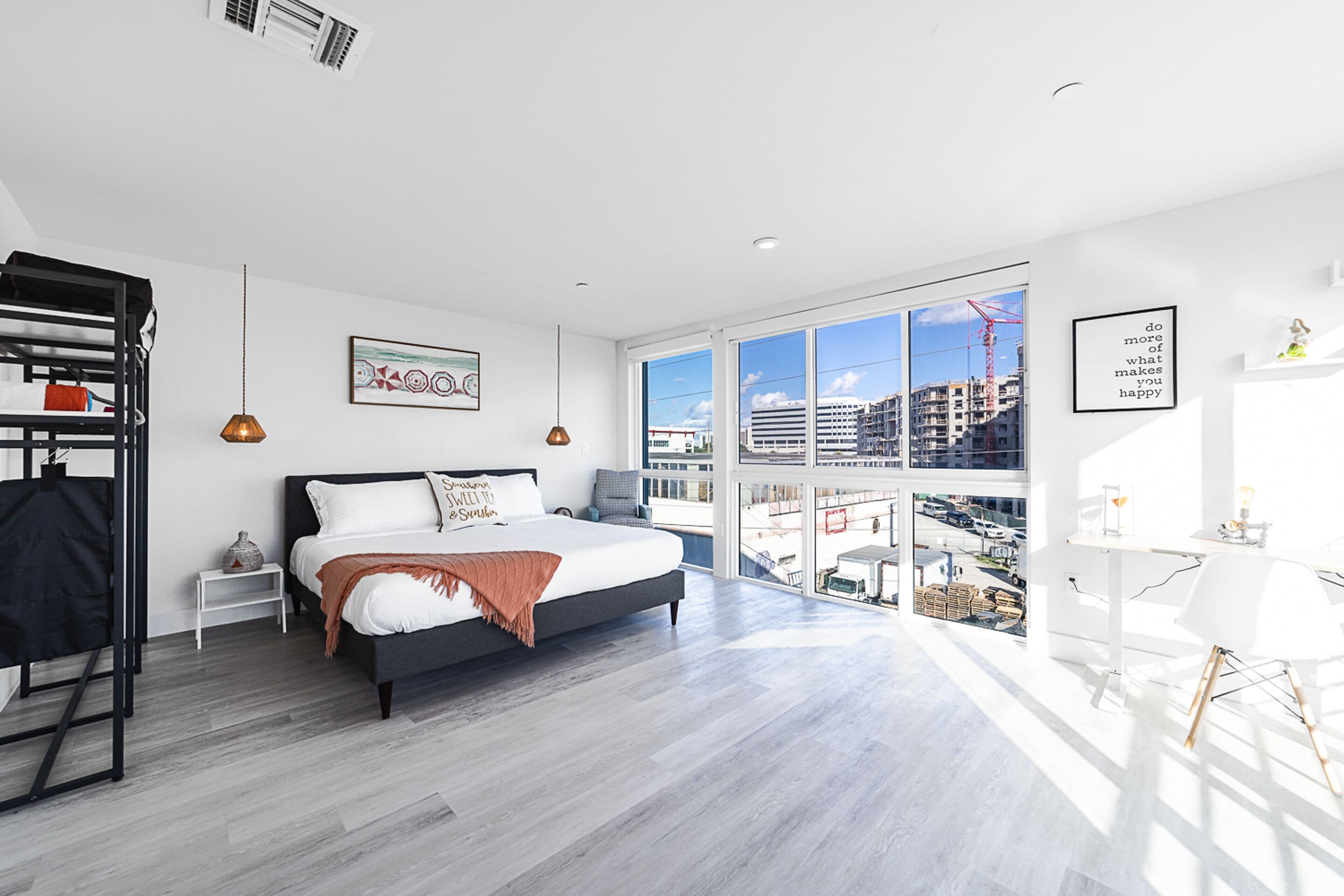 A modern bedroom with a large bed, a view of the city, and a white desk with a lamp.