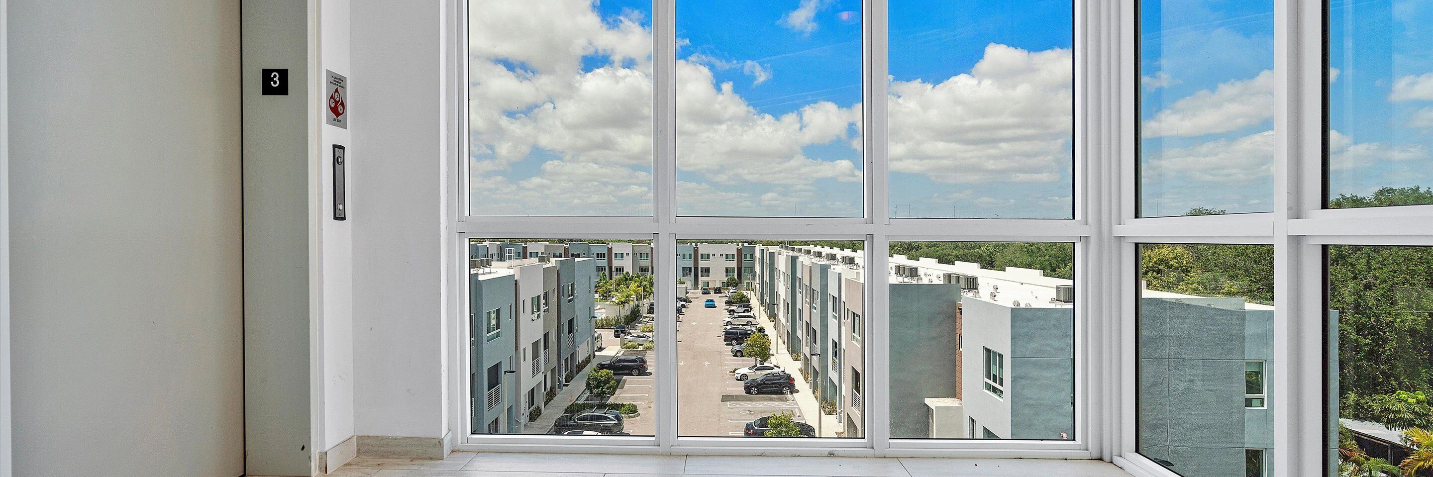 Udsigt fra et vindue i en moderne bygning, med klart himmel og parkeringsplads i forgrunden.
