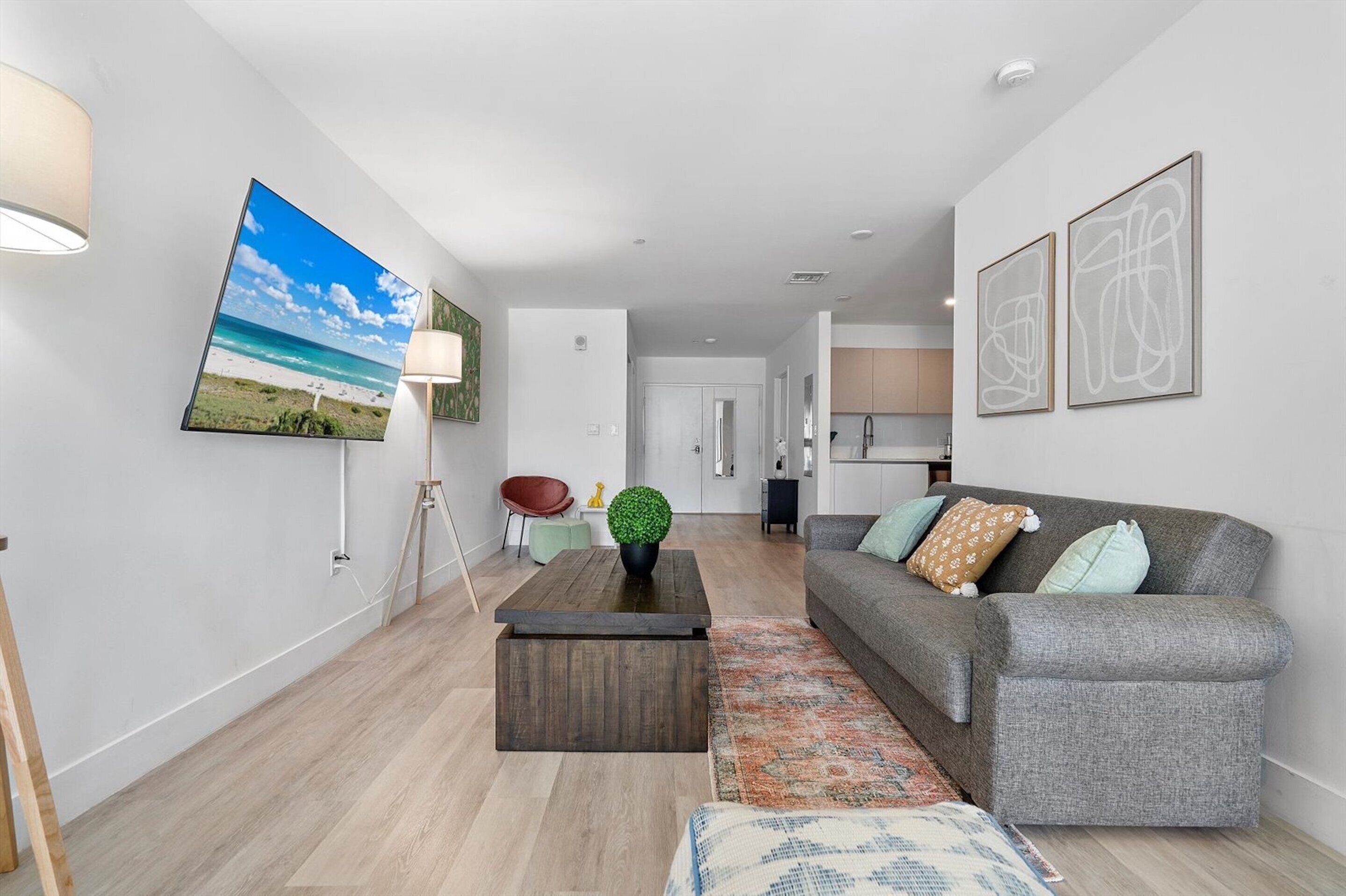Ein modernes Wohnzimmer mit einem grauen Sofa, einem Couchtisch und einem großen Bild mit Strandmotiv an der Wand.